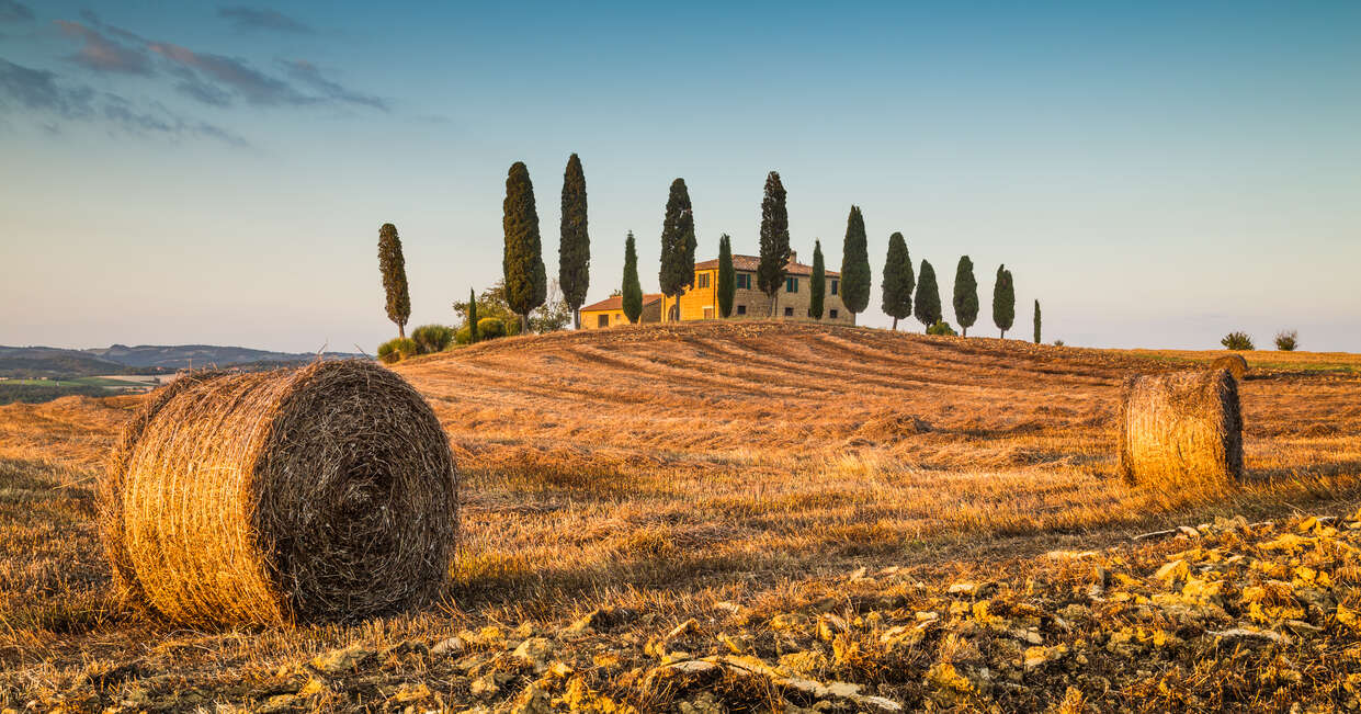 Beautiful Tuscany landscape with traditional farm house and hay bales in golden evening light, Val d'Orcia, Italy